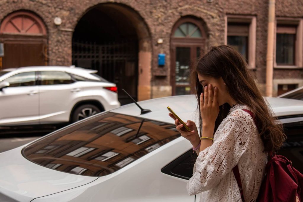Uber complaints: A woman stands by a car and looks at her phone screen