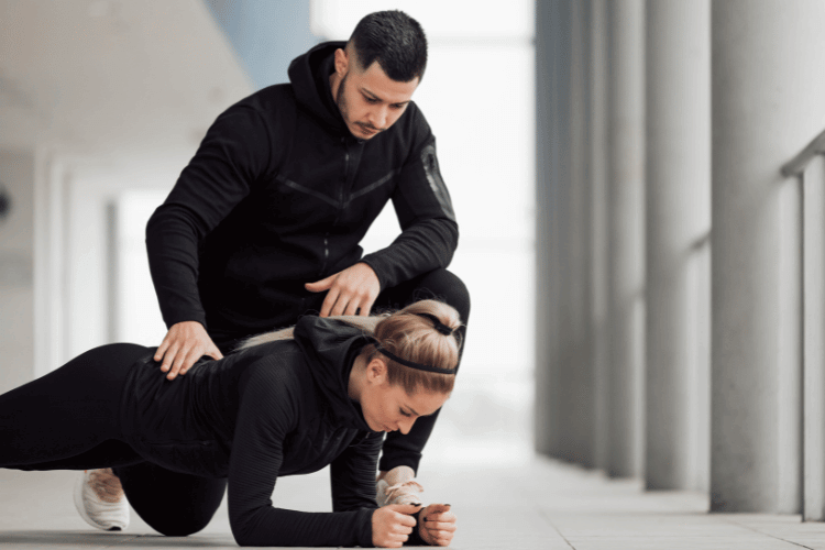 A sportswoman doing push-ups and her personal-trainer helping her 