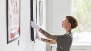 stock image showing a woman hanging art on a wall - header graphic for names for an art business post on gigworker.com