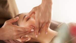 stock image showing hands at a spa massaging a woman's face - header graphic for a names for an esthetician business post on gigworker.com